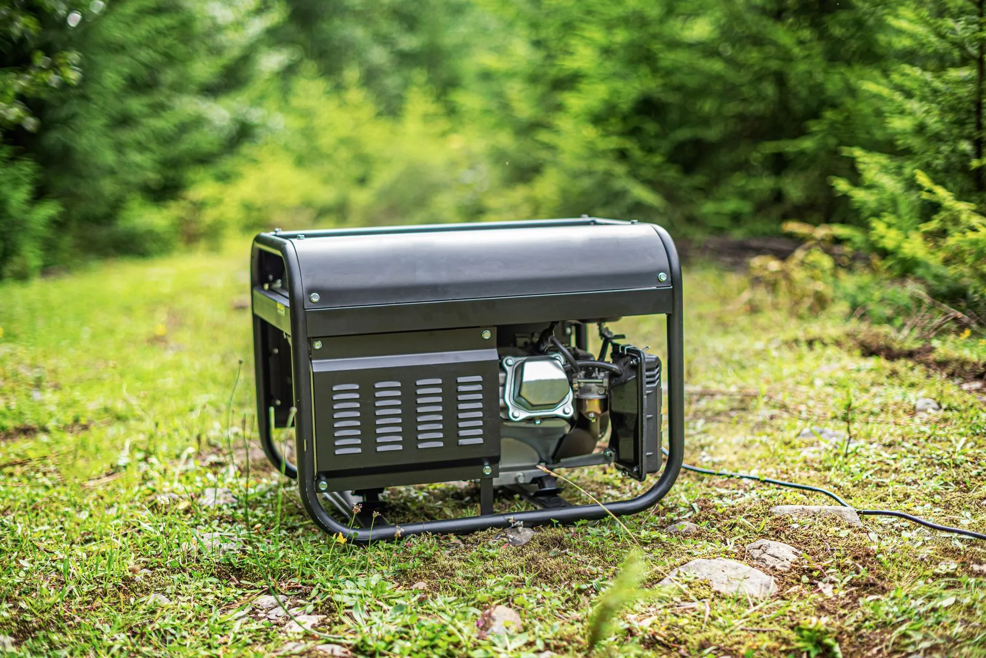 Portable gasoline generator set up on grass beside a wooded backyard
